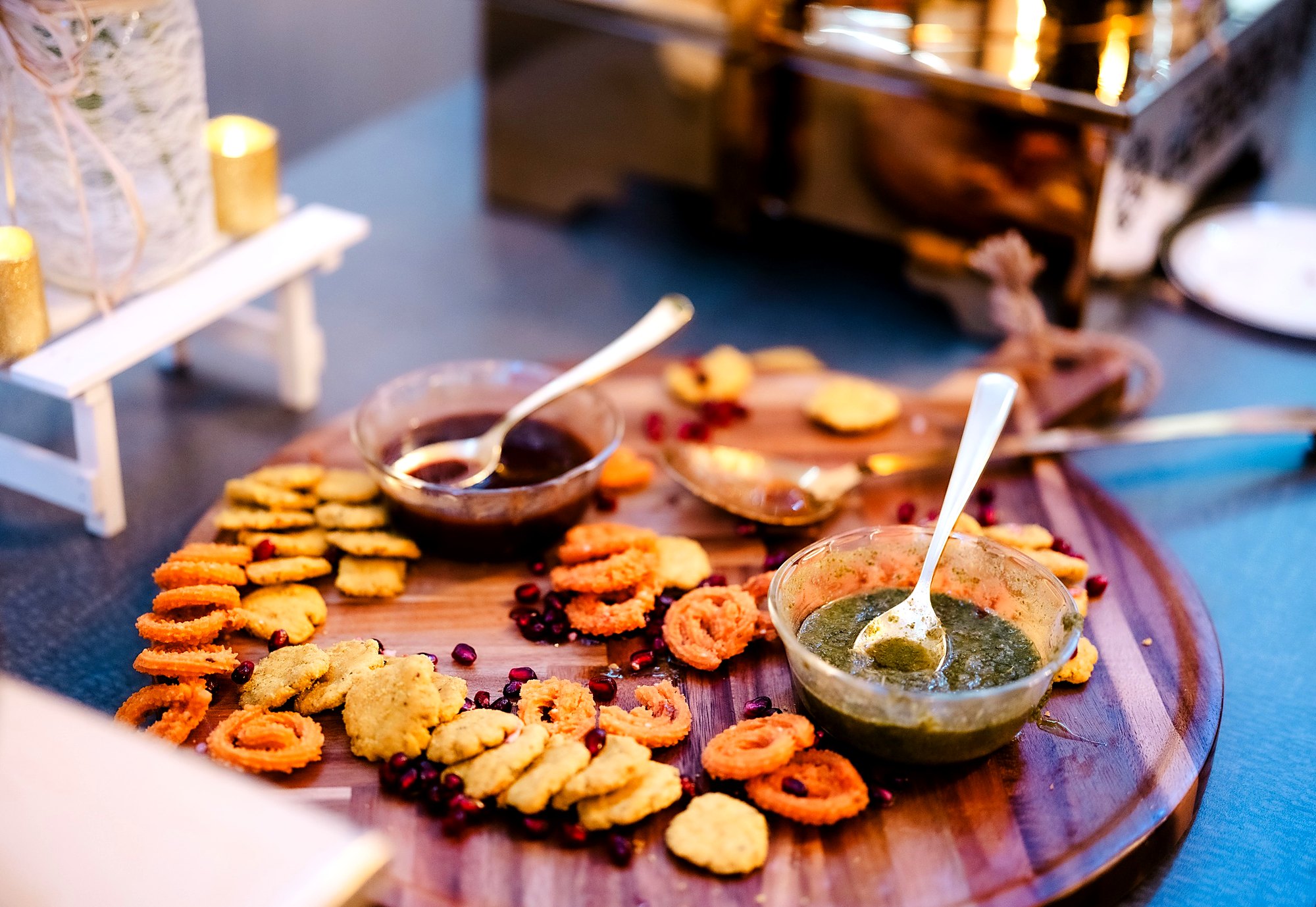 Wooden board of chakli and mathri with tamarind and mint chutneys and pomegranate seeds