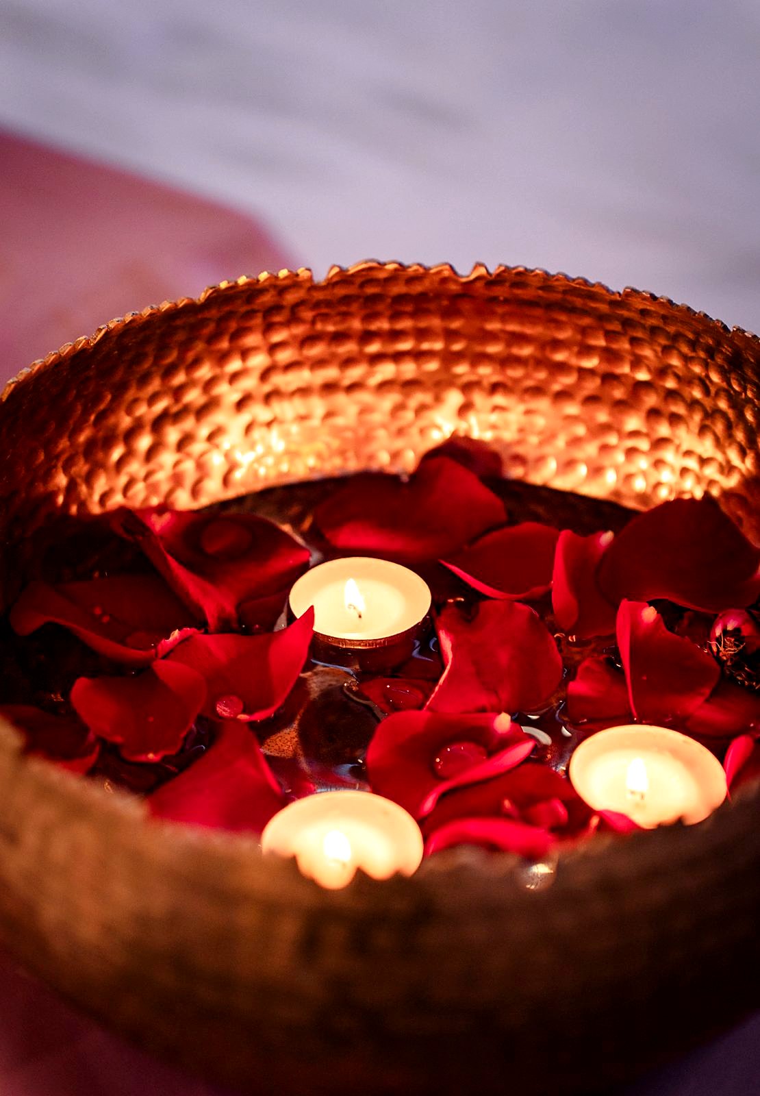 Hammered brass urli bowl with floating candles and red rose petals