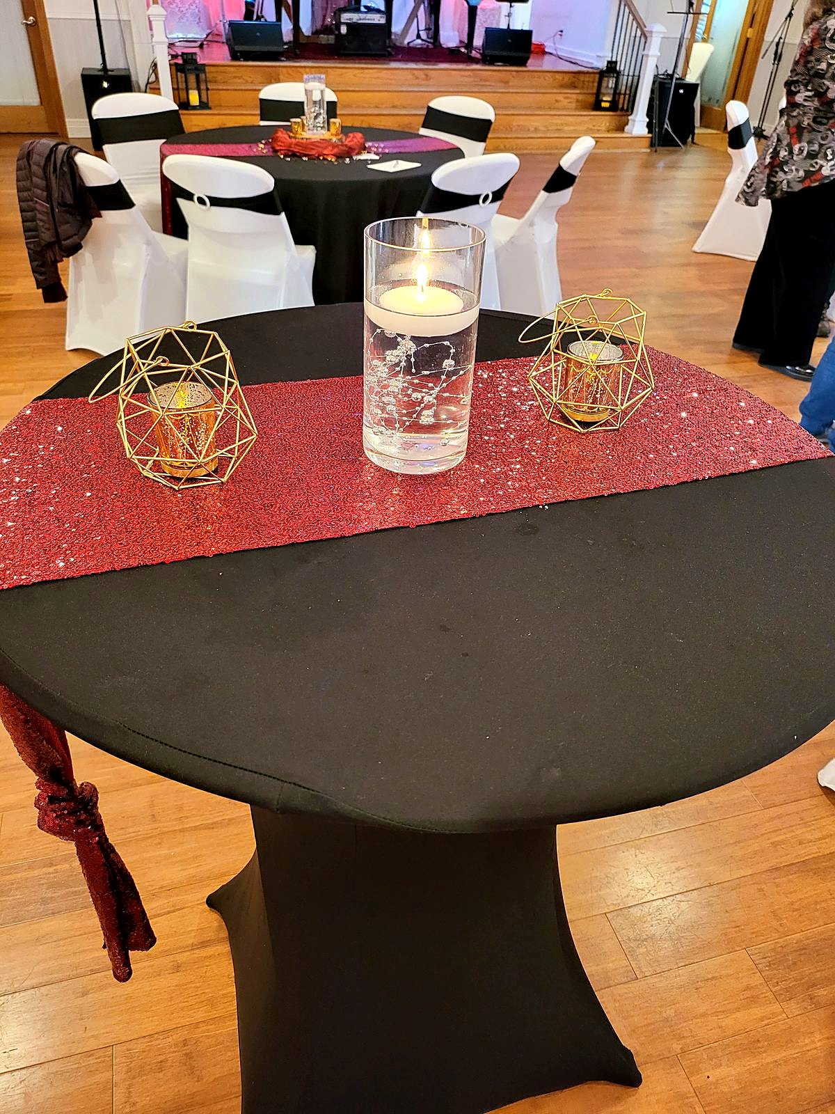 Black cocktail table with a red sequin runner, floating candle and gold geometric lanterns