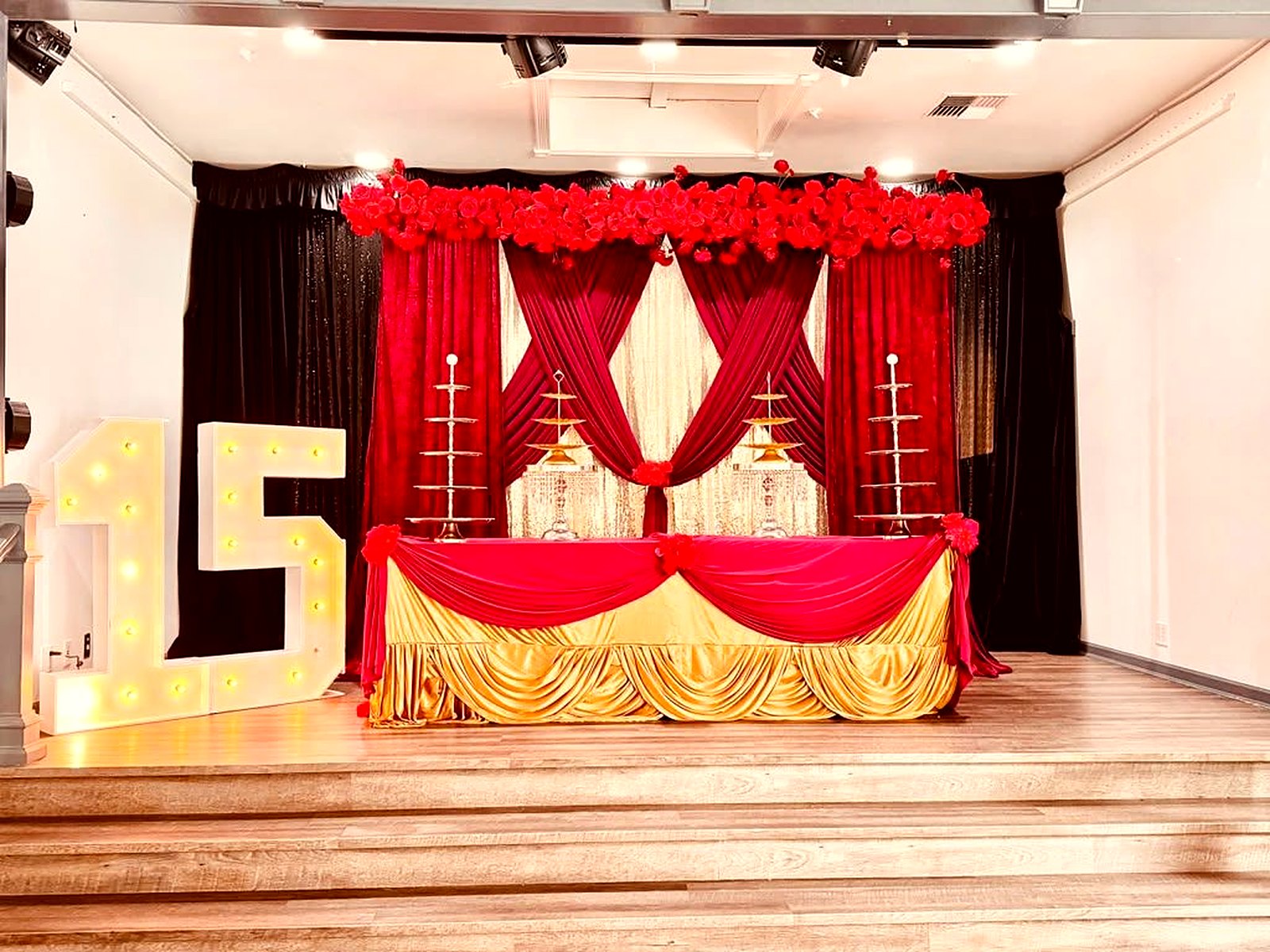Quinceañera head table – red velvet and gold drapes, red rose garland, gold dessert stands and a lit-up "15" marquee