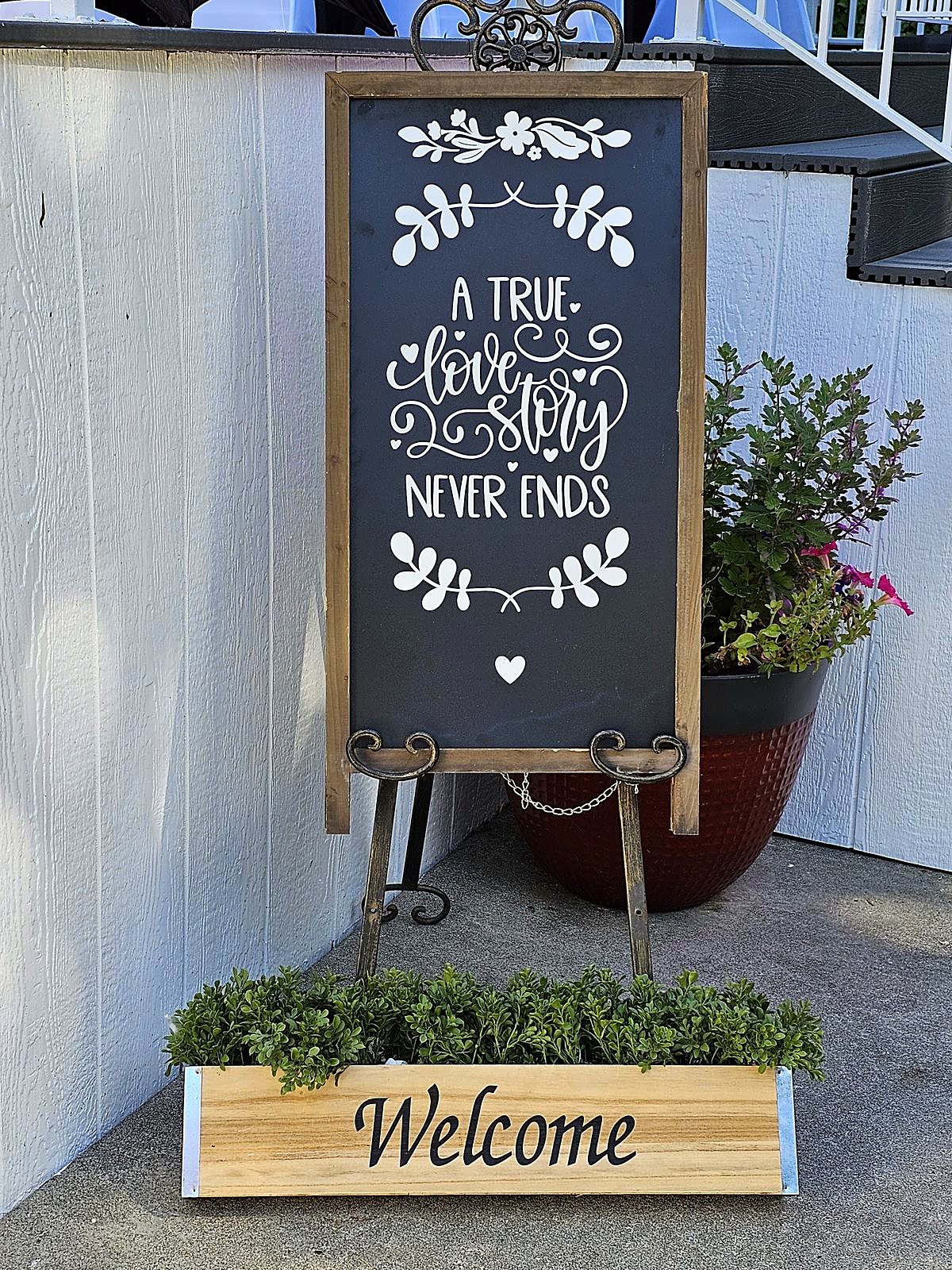 "A true love story never ends" chalkboard welcome sign with a boxwood Welcome planter