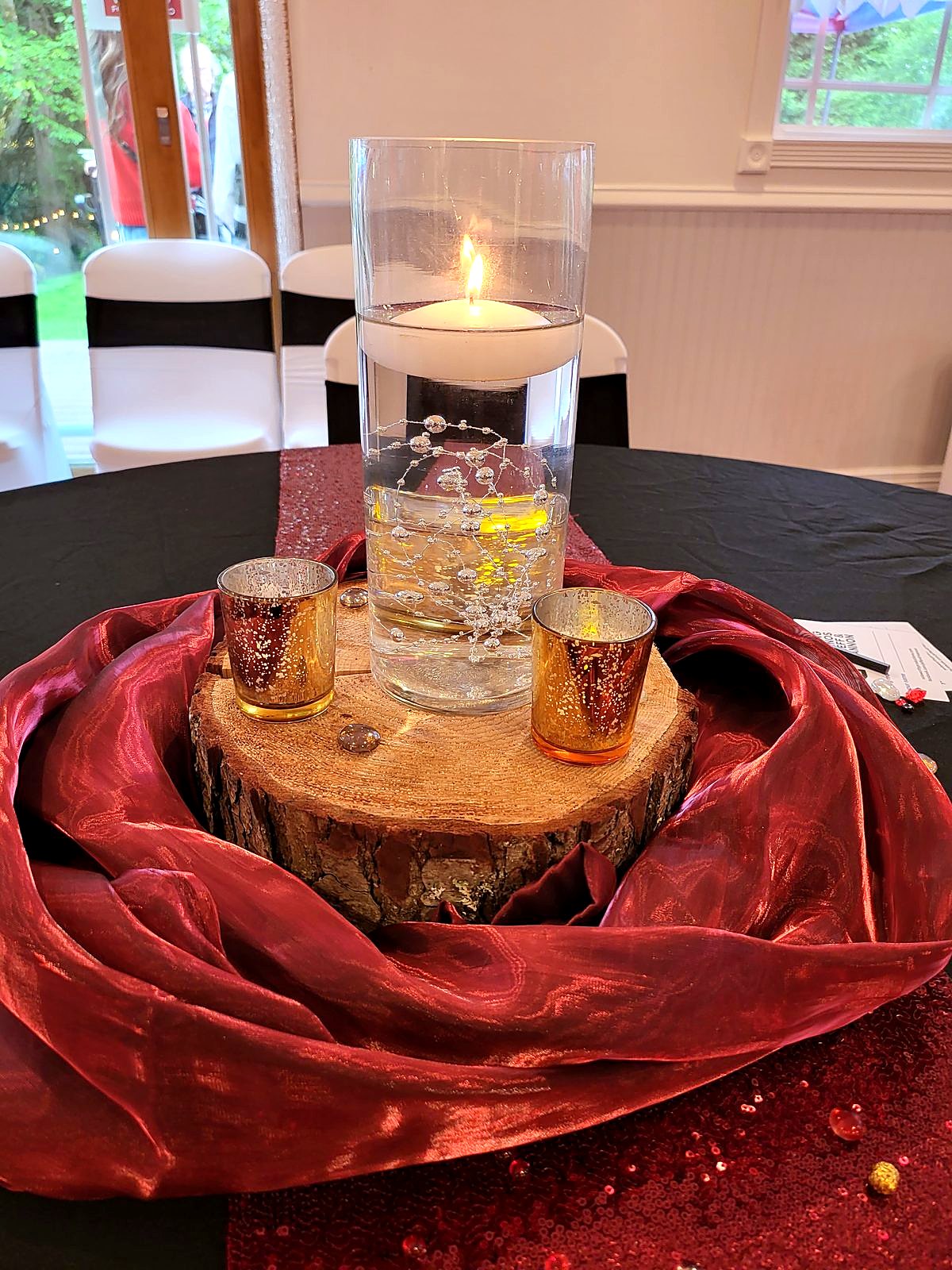 Floating candle centerpiece on a wood slice with burgundy satin and gold mercury votives