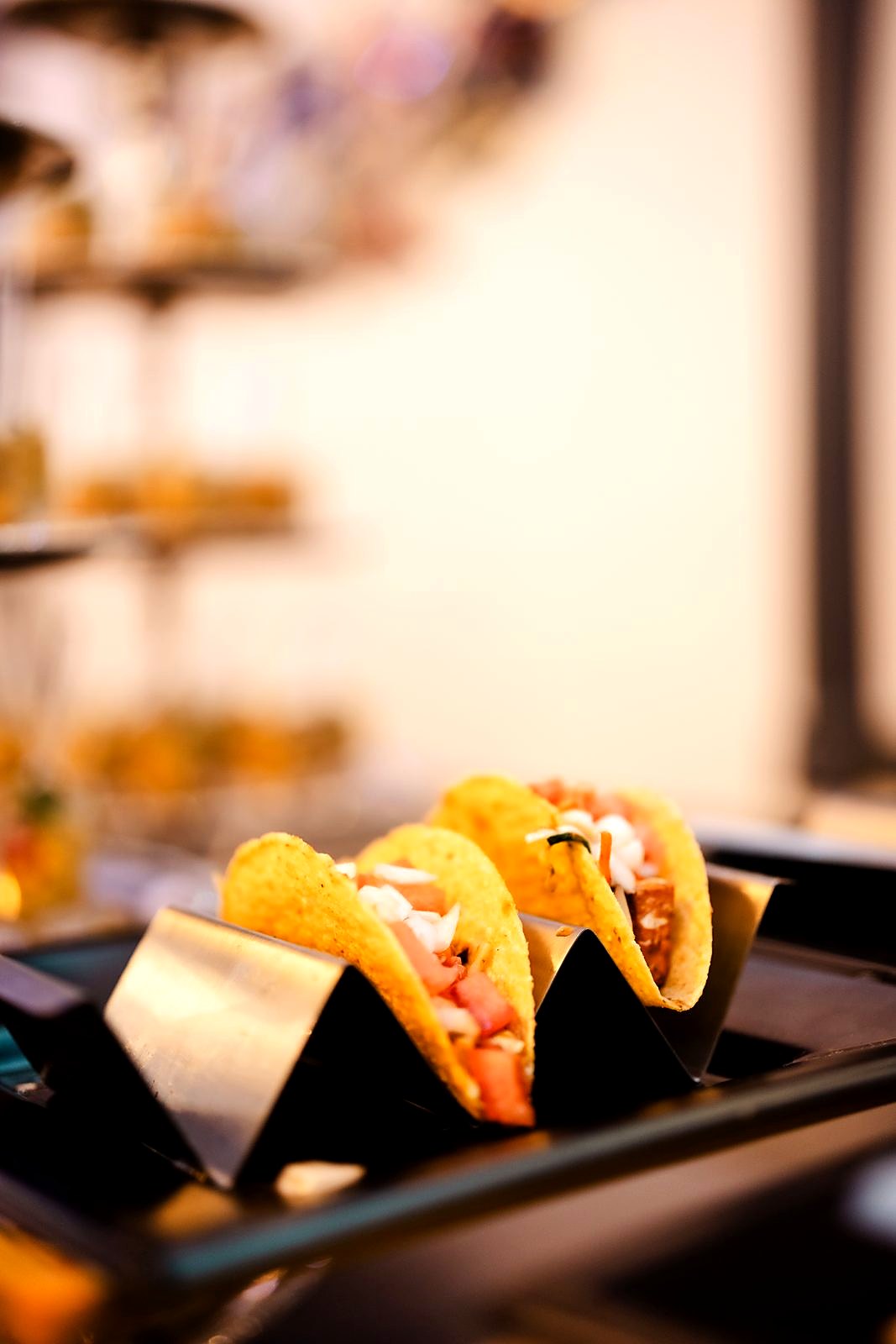 Mini crispy tacos with tomato and onion in a steel taco rack