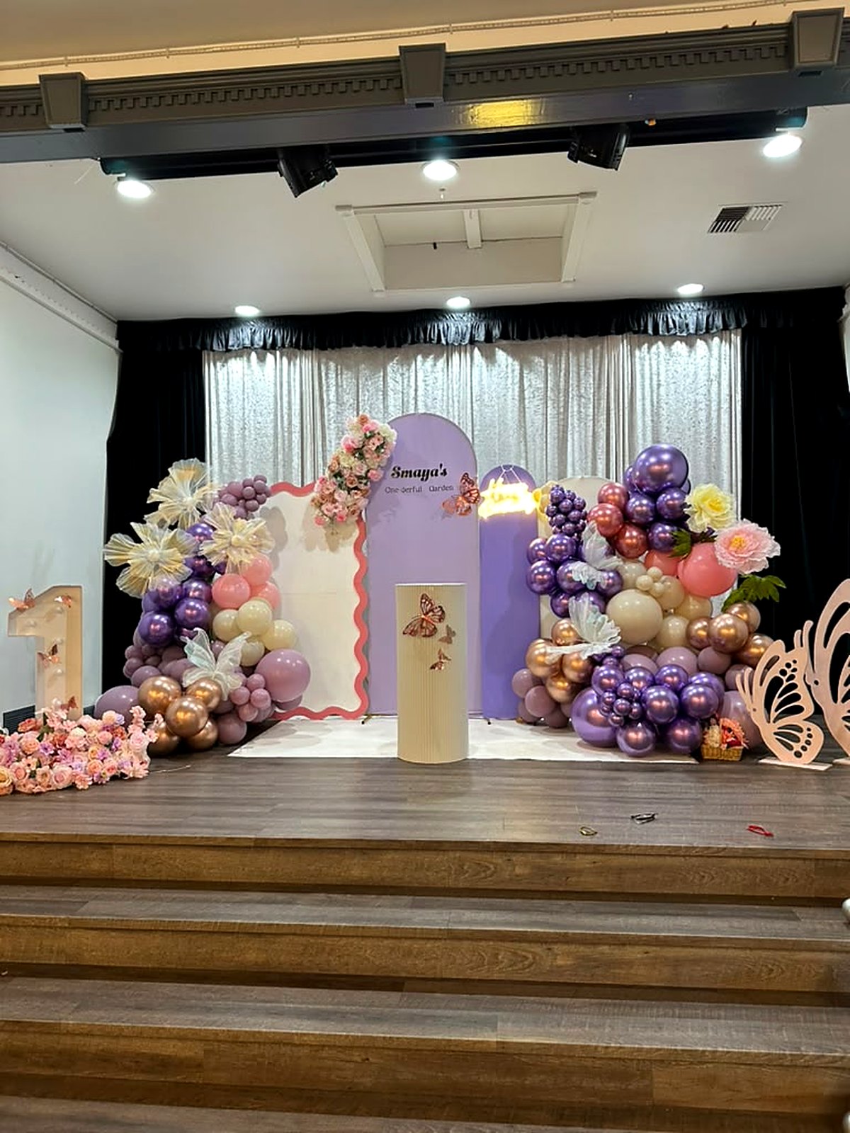 “One-derful garden” 1st birthday stage – lavender arches, butterflies, paper flowers and purple, pink and gold balloons
