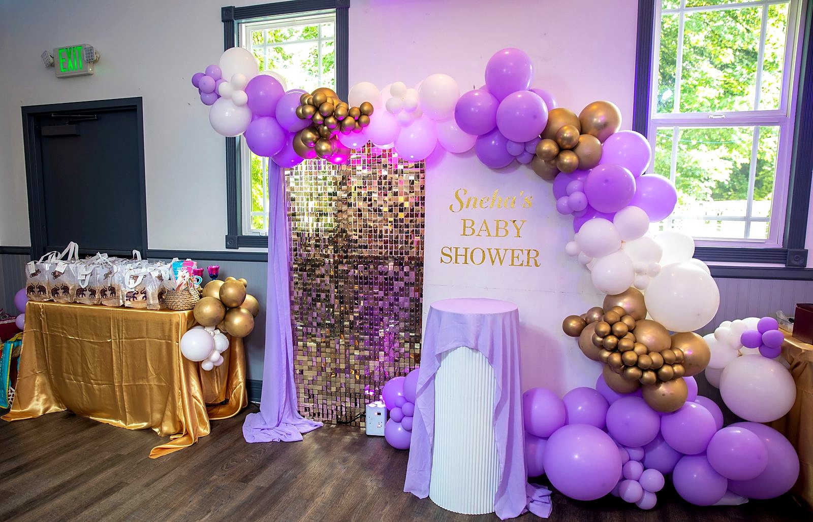 Lavender, white and gold balloon garland around a gold sequin wall, with a favor table