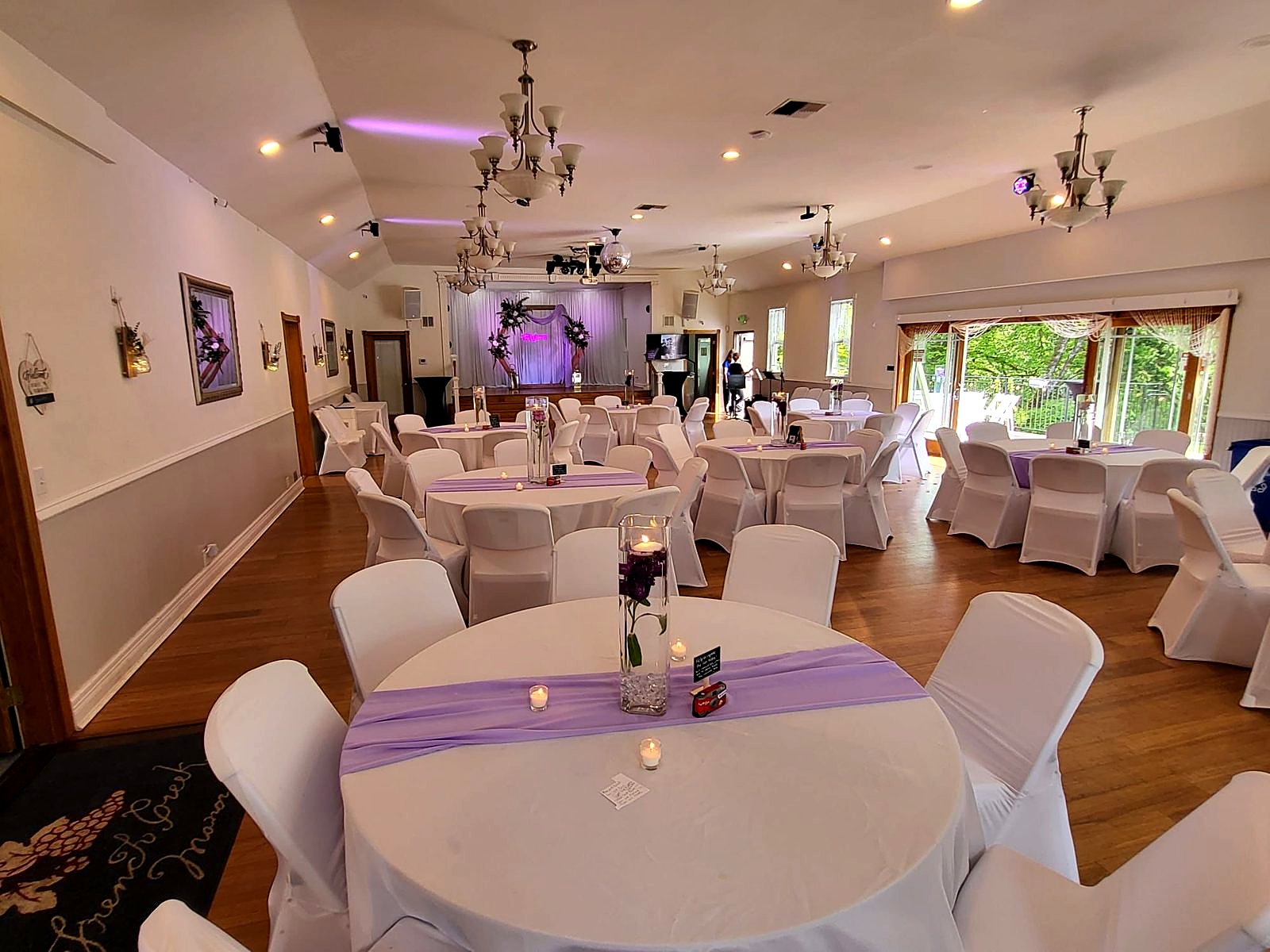 Main hall in daylight – round tables with lavender runners and floating-candle centerpieces, doors open to the deck