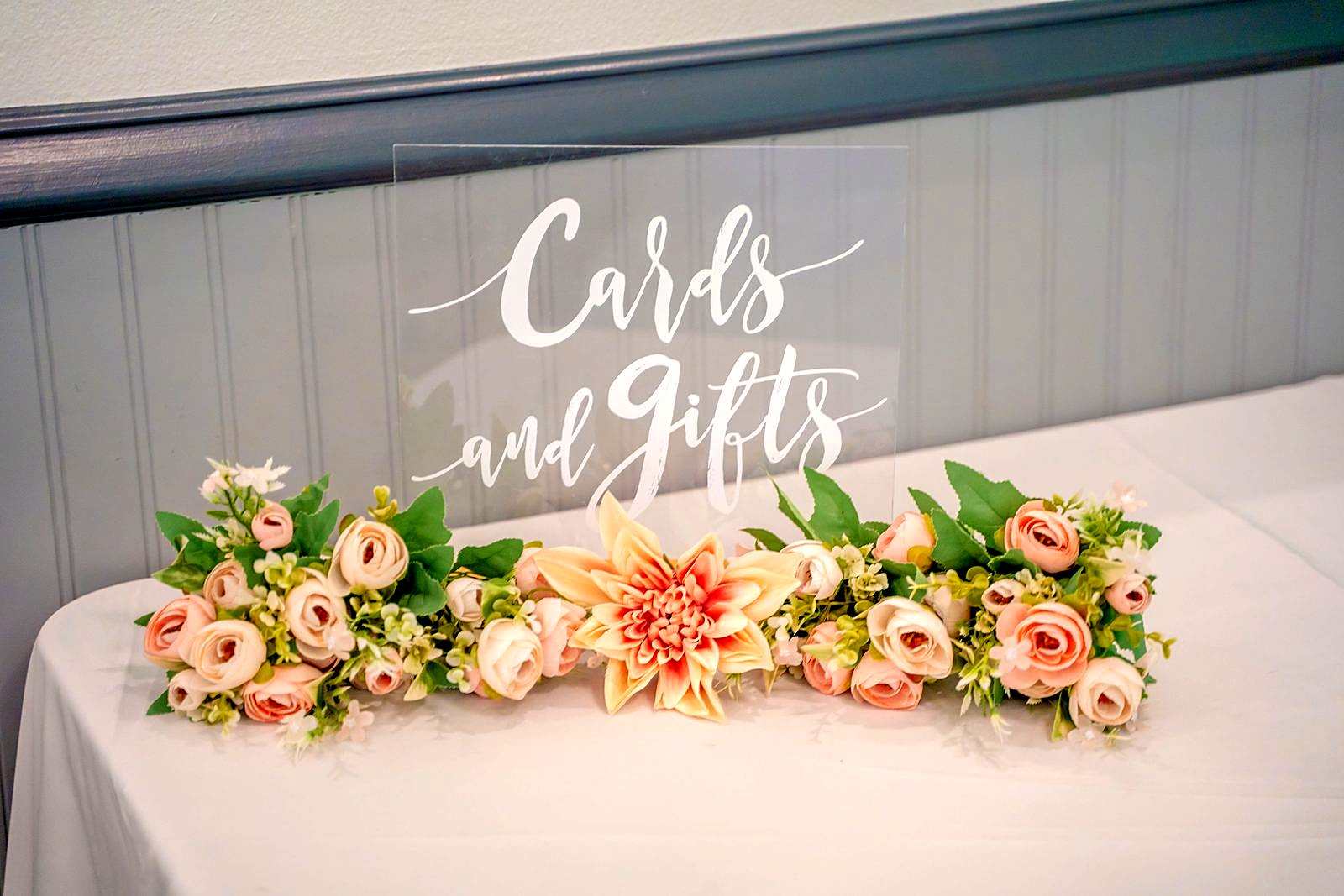 "Cards and Gifts" acrylic sign with a garland of peach ranunculus and a dahlia