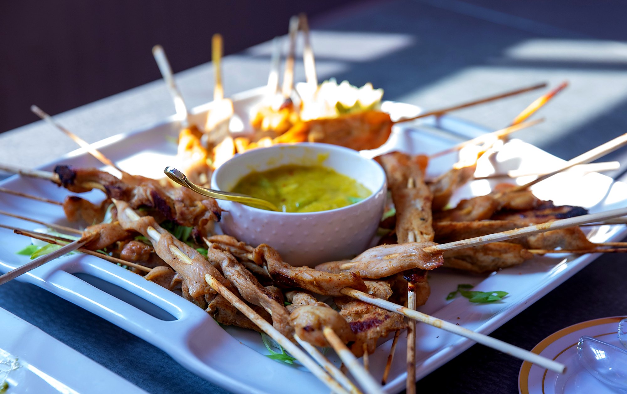 Grilled chicken satay skewers fanned around a bowl of dipping sauce
