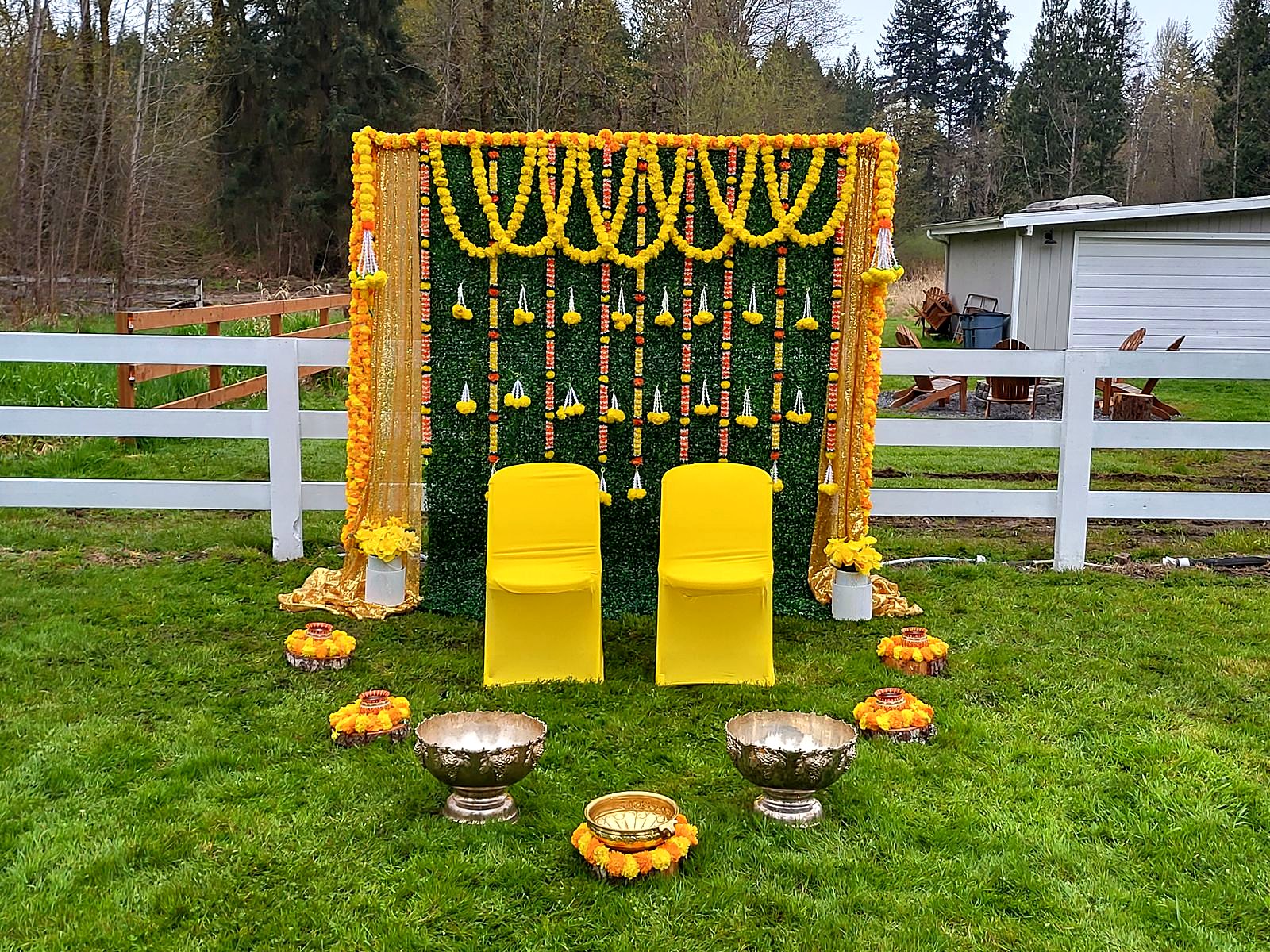 Outdoor mandap with marigold garlands and yellow chairs on the lawn