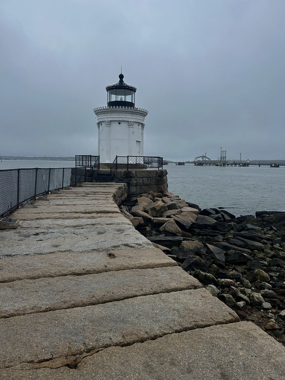 Portland Breakwater Lighthouse, a short lighthouse with Greek revival architecture and beautifully crafted columns, sits at the end of a slightly curved walkway before a blue coastal waterfront