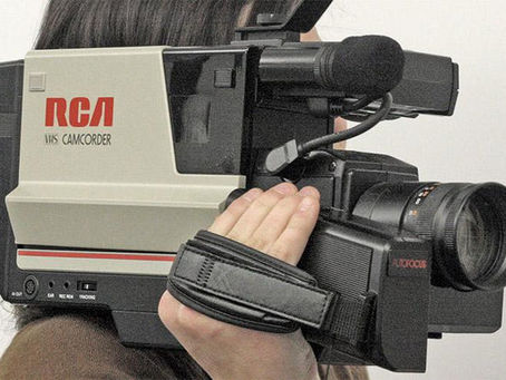 A vintage VHS camcorder is being held by a lady with dark hair, representing the VHS tape era of home movies