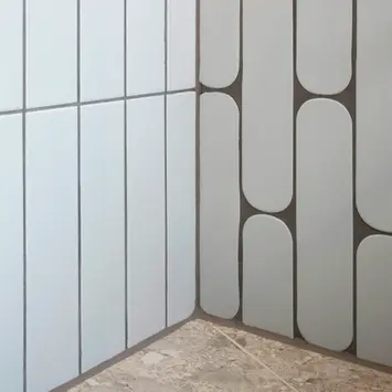 Cream tiles on two adjacent walls, with speckled beige tilw on the ground. One set of wall tiles is rectangular and the other is oblong, which is staggered. Mink coloured Grout.