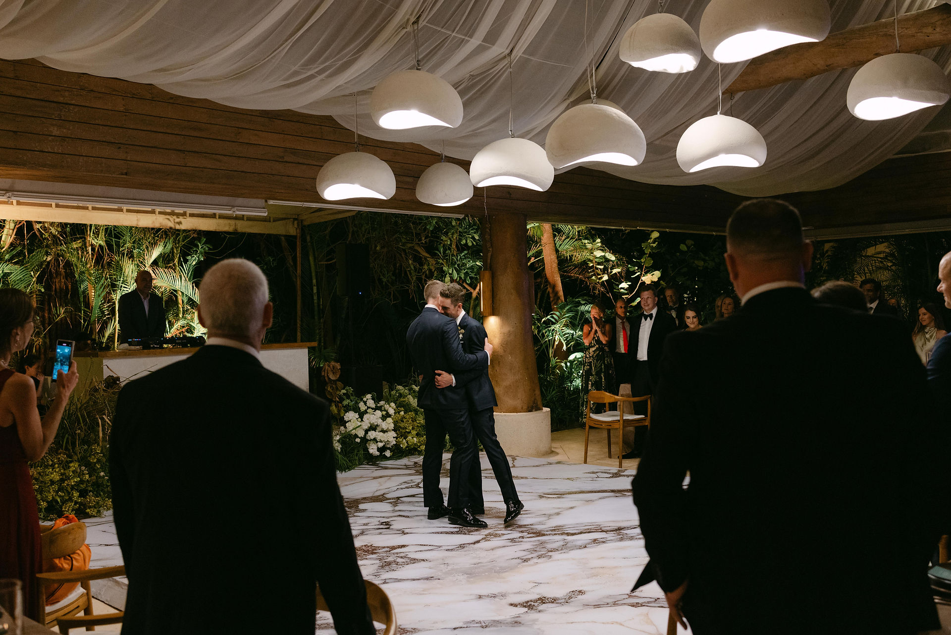 Grooms Mitchell and Craig sharing a joyful first dance surrounded by guests at their reception at Rosewood Mayakoba, designed by Canteiro Weddings and photographed by Luxart Wedding Studio.