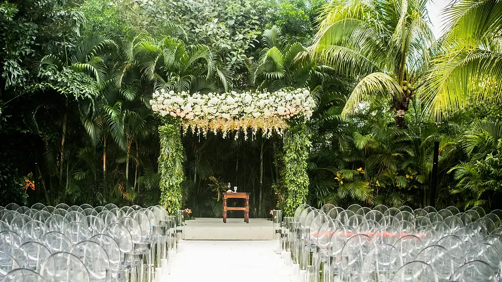 An elegant outdoor wedding ceremony in a lush tropical garden at Rosewood Mayakoba. The setup features clear ghost chairs and a white floral altar framed by a verdant foliage archway, showcasing the sophisticated and organic design possibilities at this premier Rosewood Mayakoba wedding venue.