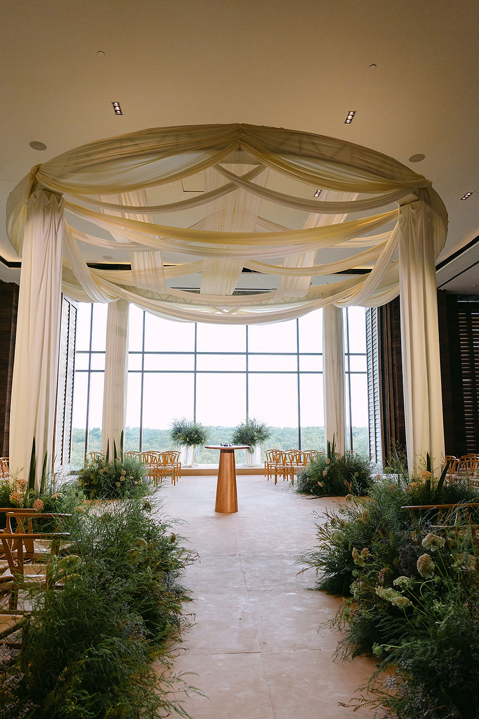 Elegant indoor wedding venue with white draped canopy, wooden chairs, greenery, and a small podium for a luxury destination wedding rain plan in Mexico.