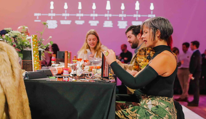 Event attendees seated at tables making kaleidoscopes, with a woman in patterned dress in foreground working with materials while others engage in the activity against a purple branded backdrop.

Creative Director: Chloe Greene
Art Director: Jordan Vouga