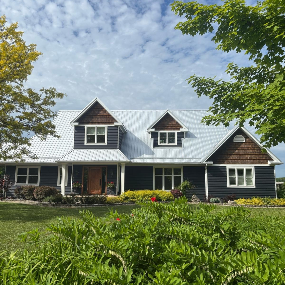 Two-story home with dark gray metal roof, front porch, and dormer windows.