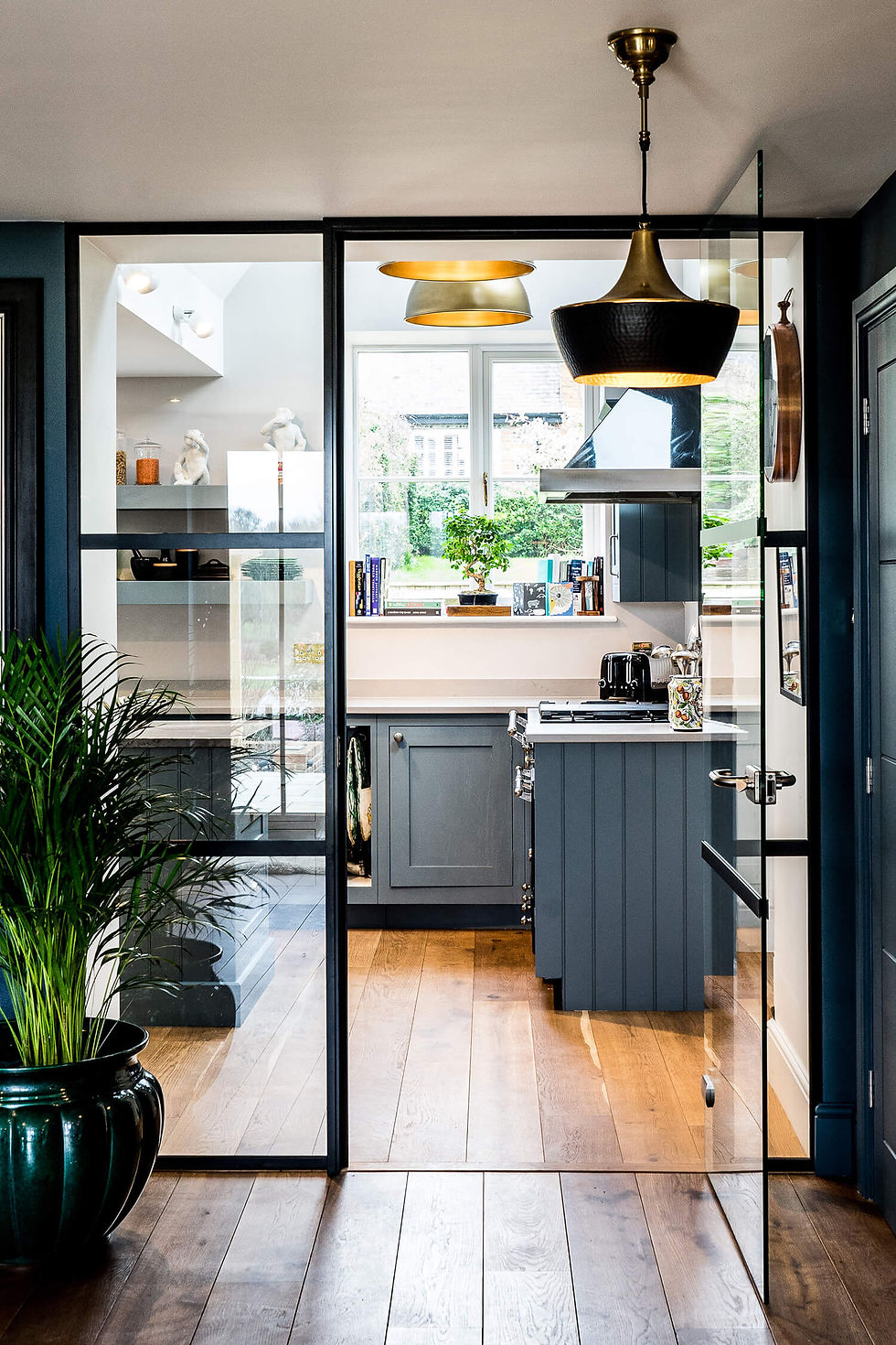 Traditional style kitchen with a modern twist, featuring a hand-painted shaker kitchen in dusky blue with quartz outer edges and a granite island. The space boasts engineered oak floorboards and a stylish glass partition for an open-plan layout.