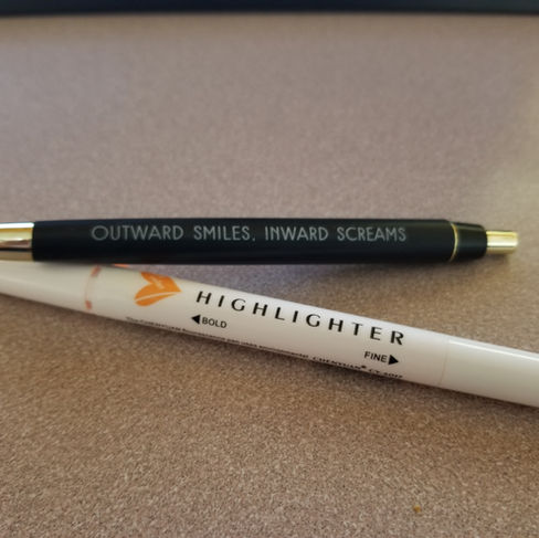 a black pen that says "Outward Smiles, Inward Screams" and an orange highlighter on a desk