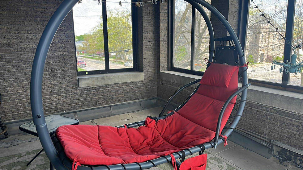 Bobbi's red-cushioned hammock chair on a porch with brick walls, overlooking a street through large screened in windows.