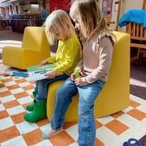  Two little girls reading on the children's floor while sitting in a comfy yellow chair