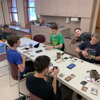 A group of teens gathered around a table playing a card game