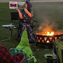 Melissa Snow reading a storybook dressed as a witch outside in front of a fire.