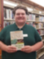 Kyle holding a copy of The Green Mile by Stephen King in front of the book shelves of the library