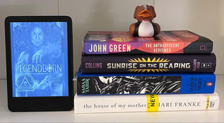 a stack of books with a rubber ducky on top with a kindle propped up to the side