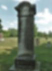 Tall, weathered gravestone with "Twist" inscription in cemetery. Cloudy sky, distant trees, evokes solitude and reflection.