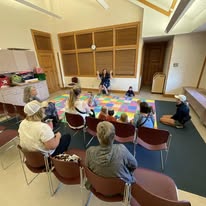 Melissa Snow sitting in a chair reading a story to a group of children circled around her