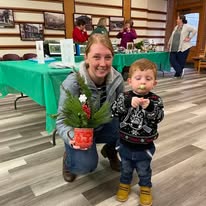A mom and her son showing off her evergreen arrangement in a red coffee cup