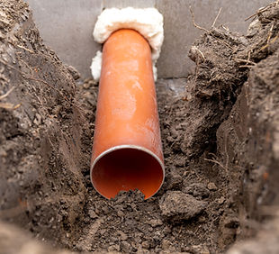 An orange plastic drainage pipe emerges from a narrow trench, surrounded by rough, freshly