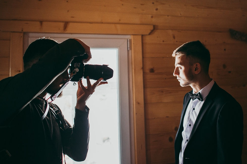 wedding photographer taking a picture of the groom in front of a brightly lit window