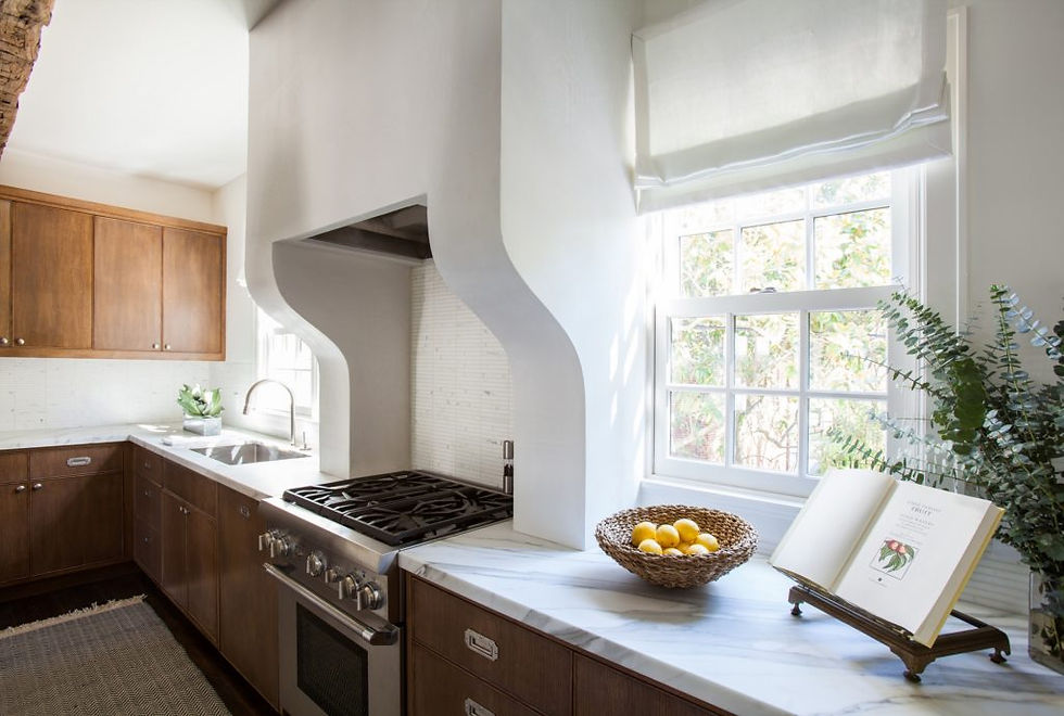 Bright kitchen with wood cabinets, marble countertops, and a window. A basket of lemons and an open book decorate the counter. Peaceful mood.