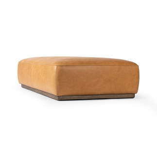 Low upholstered ottoman in warm camel tones with soft rounded edges