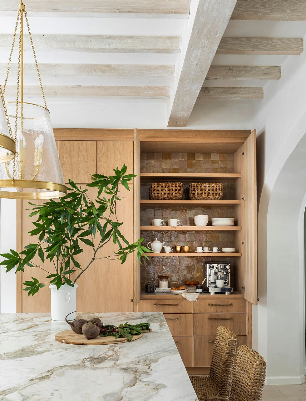 Kitchen with marble countertop, wooden cabinets, open shelves holding cups, teapots, a coffee machine, and greenery in a vase. Cozy ambiance.