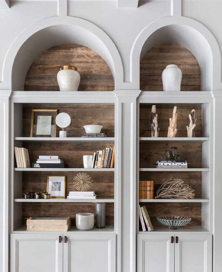Arched shelves with books, vases, framed photo, and decorative items against a wooden backdrop. Neutral tones create a calm, elegant mood.