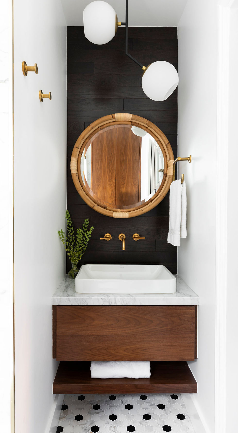 Modern bathroom with a round mirror, wooden vanity, and marble countertop. Black-and-white hexagon tile floor, gold fixtures, and white towels.