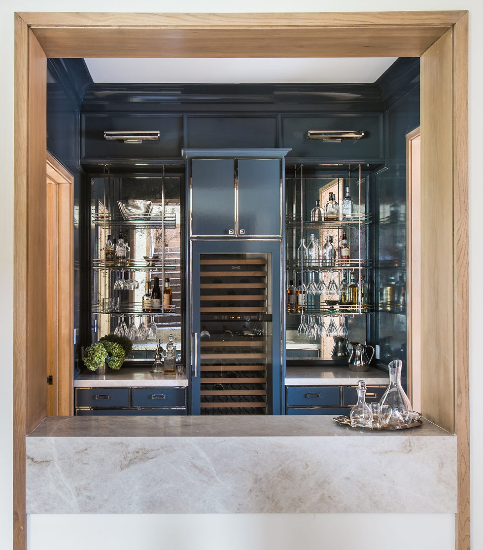 Elegant home bar with dark blue cabinets, glass shelves displaying bottles and glasses. Marble countertop in the foreground. Luxurious setting.