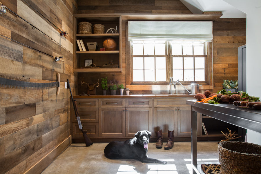 Rustic kitchen with wooden cabinets, wall, and hunting decor. A black dog rests on the floor. Fresh vegetables on a table. Cozy ambiance.