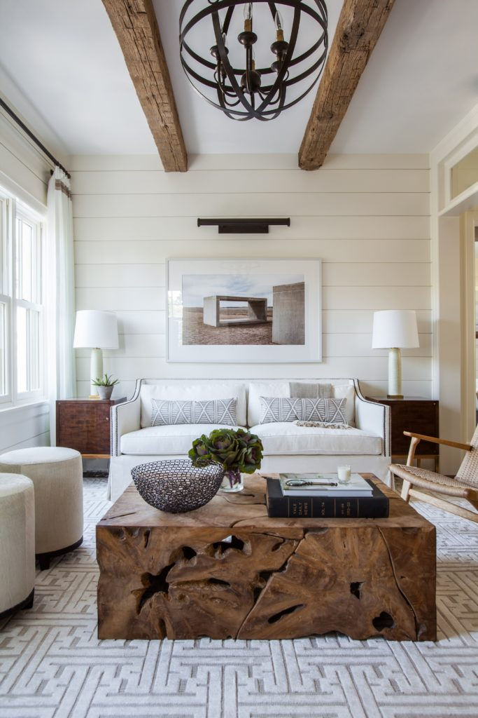 Cozy living room with a white sofa, wooden coffee table, and geometric rug. Rustic beams and chandelier above, with modern decor elements.