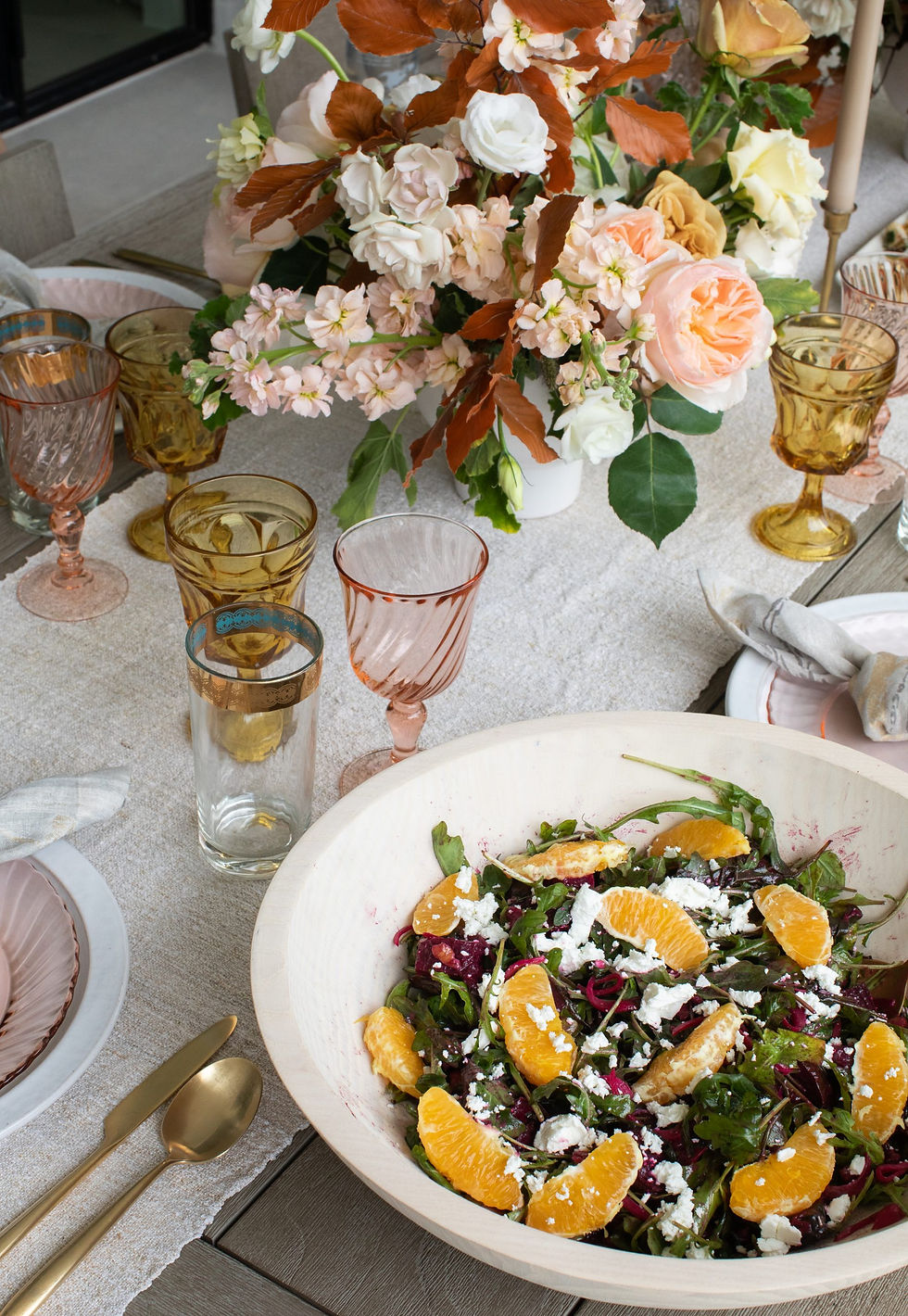 Elegant table setting with colorful flower centerpiece, orange salad in a bowl, gold cutlery, and vintage glasses on a linen tablecloth.