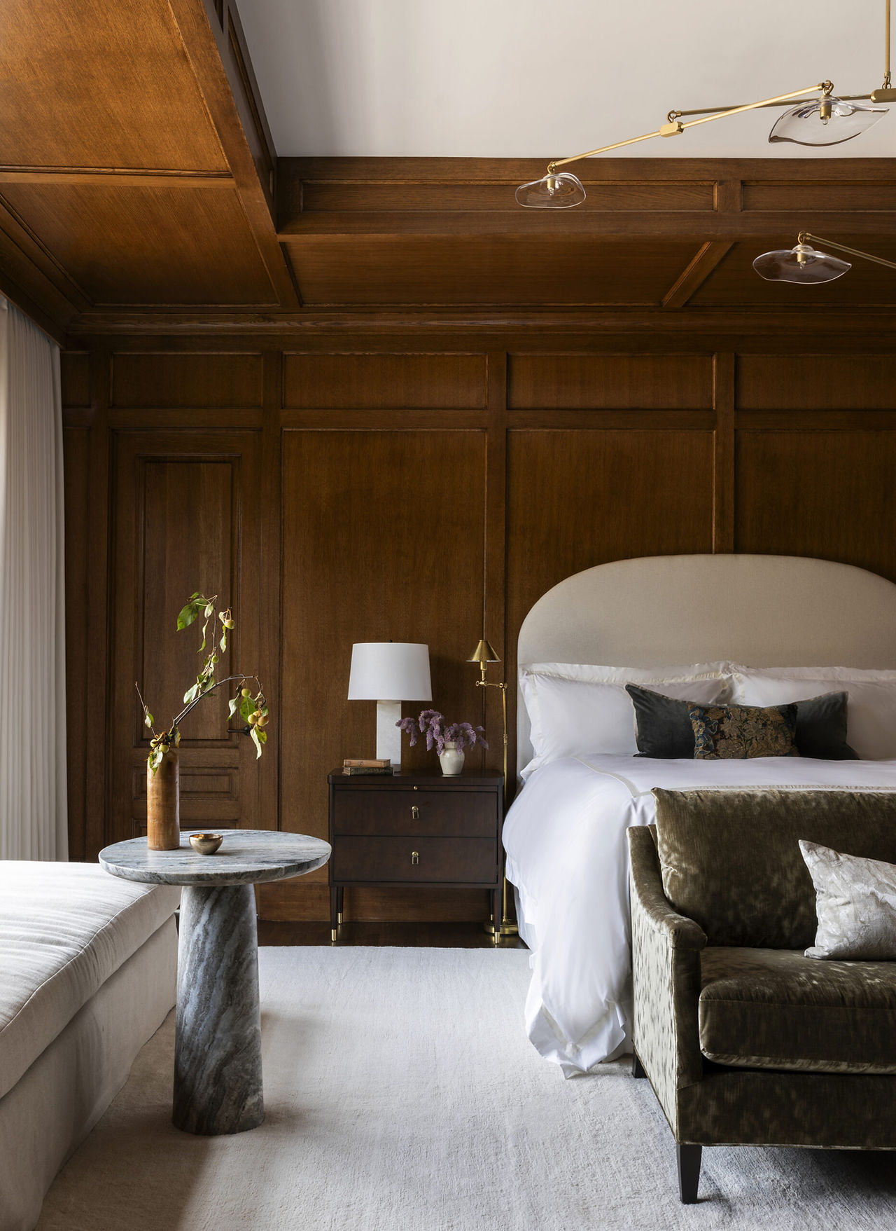 Luxury primary bedroom with custom bed, wood paneled walls, sculptural lighting, and layered textures