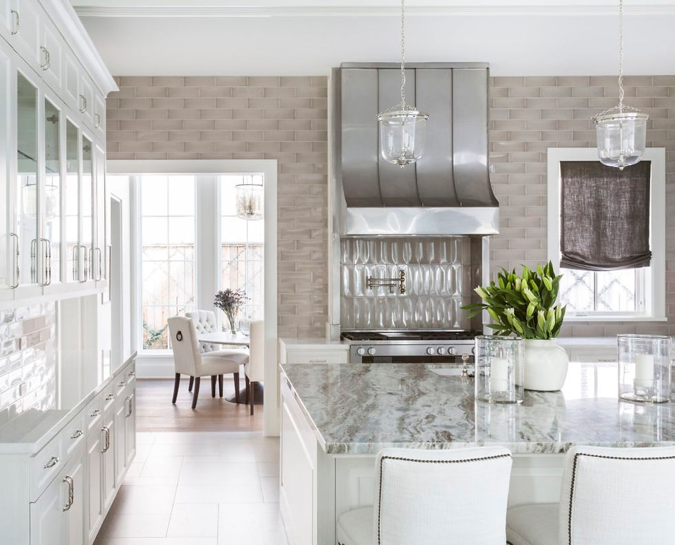Bright modern kitchen with marble island and two white chairs. Stainless steel stove and hood. Vase with green plants. Neutral tones.