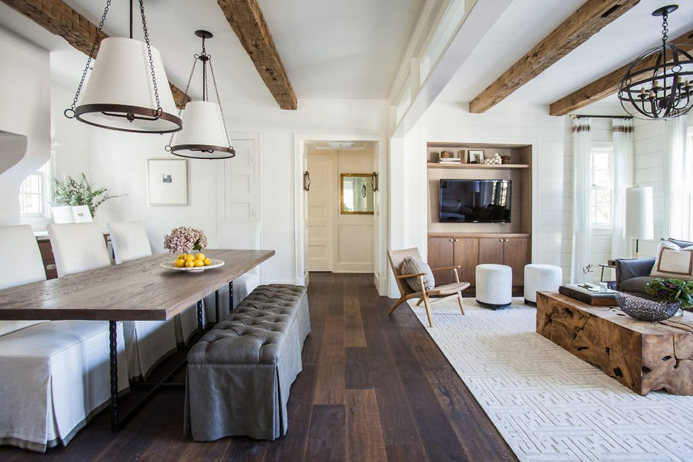 Rustic dining and living room with wooden beams, dark floor, white walls. Table set with lemons, cozy seating, and a soft ambiance.