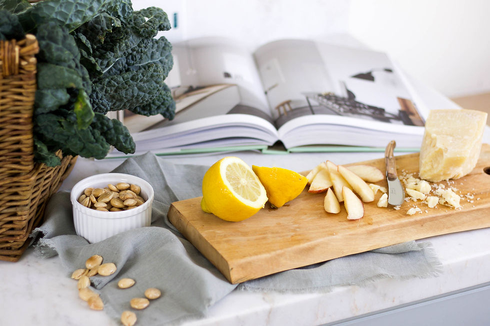 Cutting board with lemon halves, apple slices, and cheese. Open book in background. Kale in basket and almonds in bowl nearby.