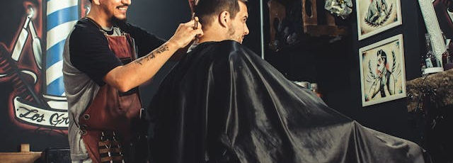 A barbershop with a male barber cutting the hair of a male client