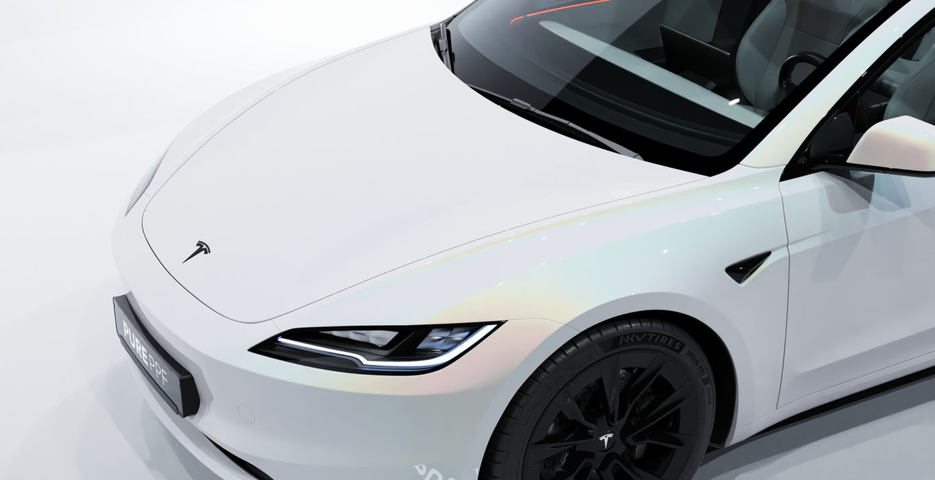 Close-up of a Tesla Model 3's front, wrapped in PurePPF Luma White, highlighting the detailed bright pure white finish with luminous rainbow effects in direct sunlight.