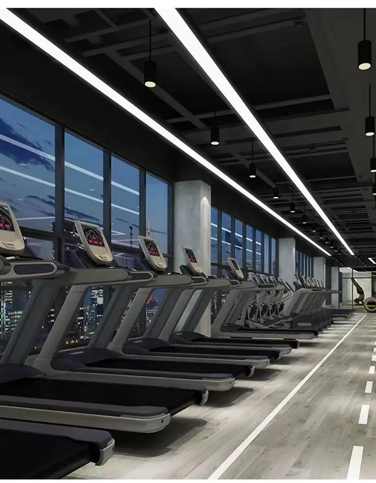 A row of treadmills facing a large wall of glass windows with LED strip lighting illuminating them. 